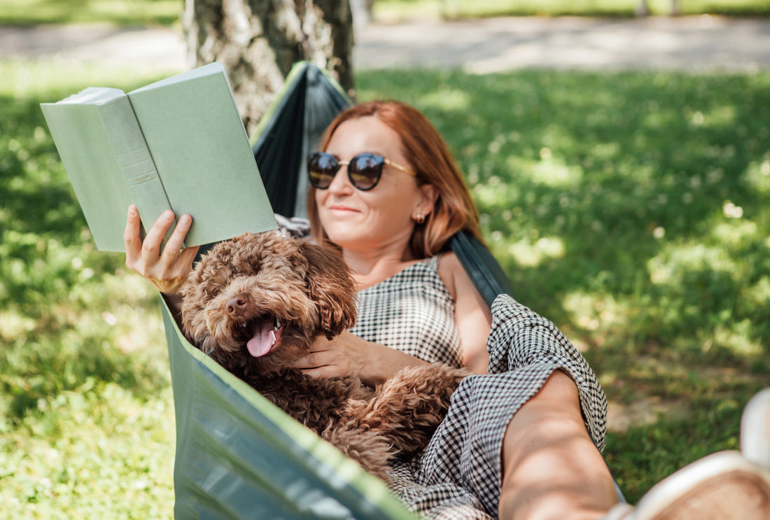 A woman reads a new release in a hammock with her dog