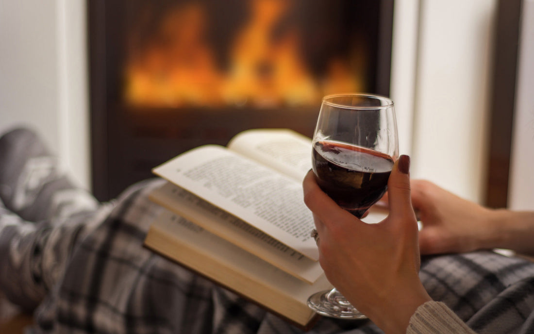 Woman reading a book in front of a fire with a glass of wine