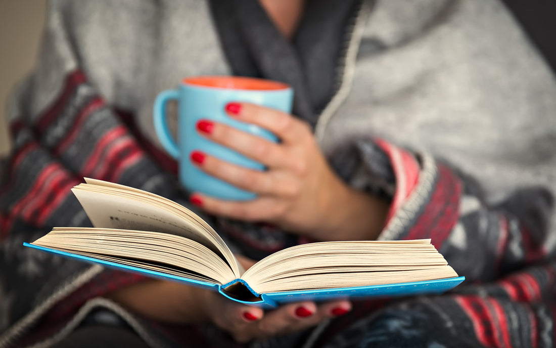 Woman holds a mug while reading a cozy October book release