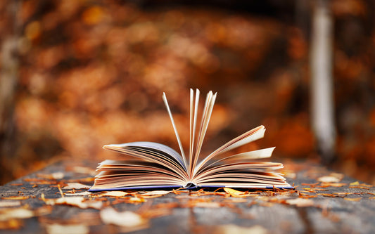 Book open in the middle of fall leaves on a table