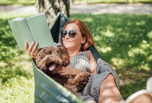 A woman reads a new release in a hammock with her dog