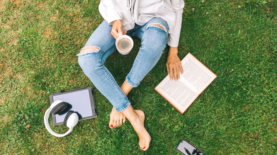 Woman sits in a park with coffee and a book